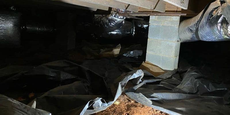 Unfinished crawlspace with exposed ductwork, concrete support piers, and a loose black vapor barrier covering the ground.