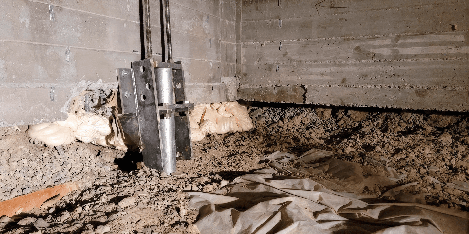 Crawlspace with exposed dirt, damaged vapor barrier, and a metal foundation support jack installed beneath concrete foundation walls.