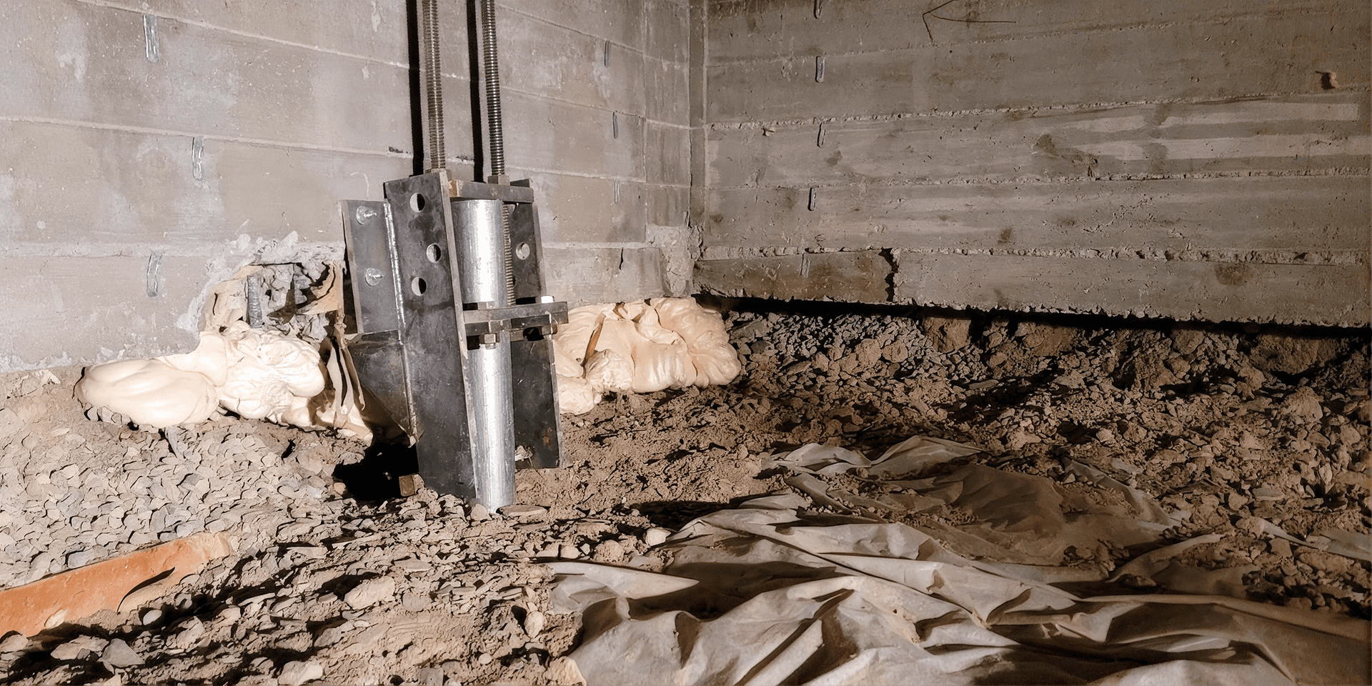 Foundation repair support pier installed beneath a concrete foundation wall in an unfinished crawlspace.