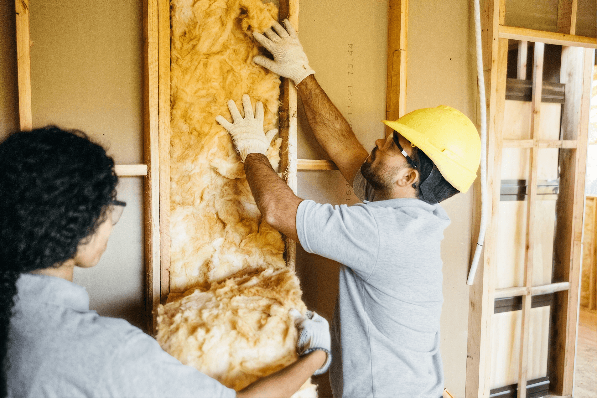 Workers installing fiberglass insulation between wall studs during a home insulation project.