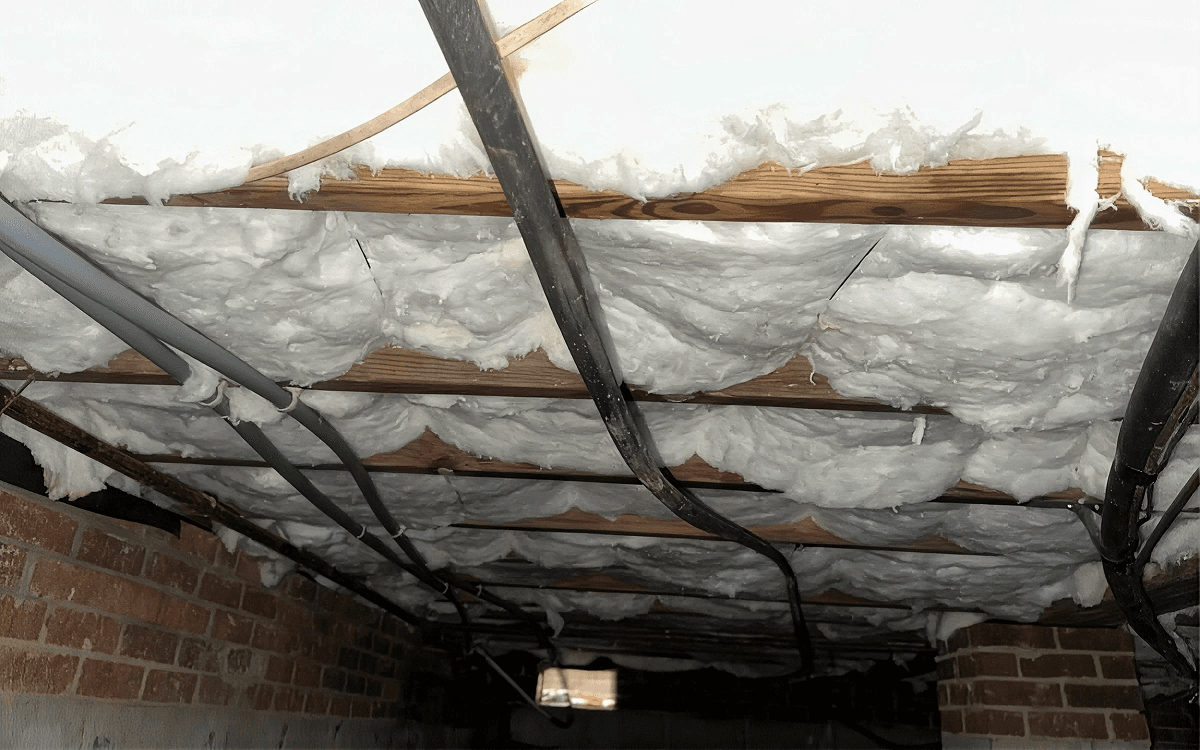 Close-up of a crawl space ceiling with fiberglass batt insulation securely installed between floor joists, helping improve energy efficiency and indoor comfort.