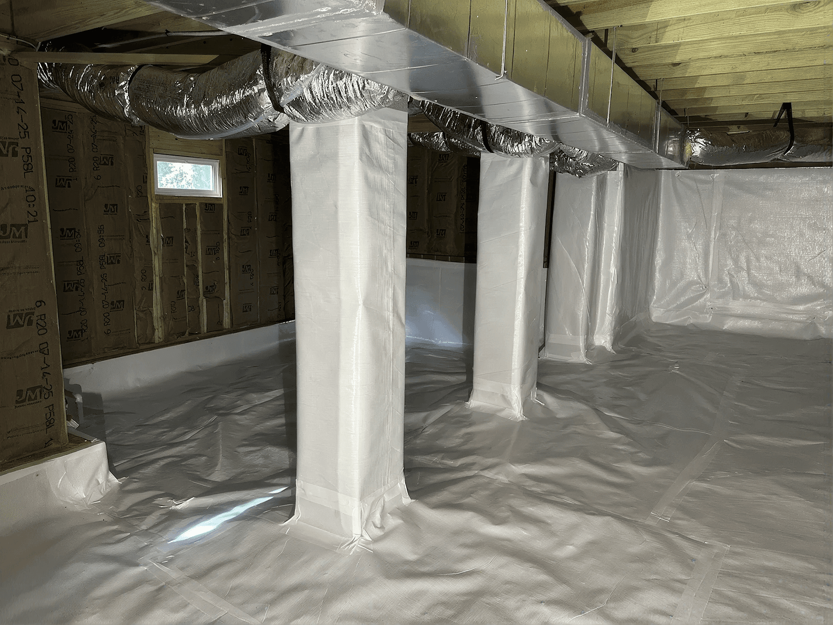 Encapsulated crawl space with a sealed white vapor barrier covering the floor, foundation walls, and support columns, along with exposed HVAC ductwork and floor joists, creating a clean, dry, and moisture-controlled under-home environment.